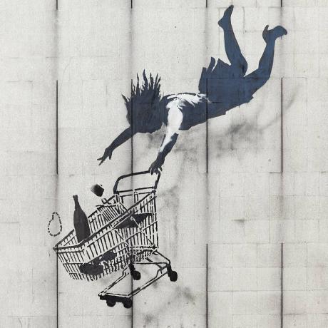 Banksy 스텐실은 쇼핑 카트와 함께 떨어지는 여성을 보여줍니다.