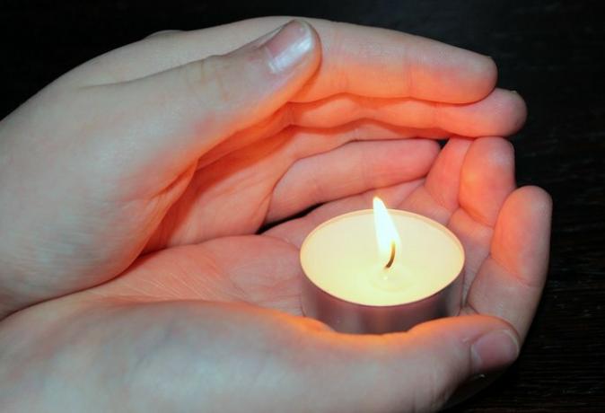 ръце, държащи свещ и получаващи радиационна топлина